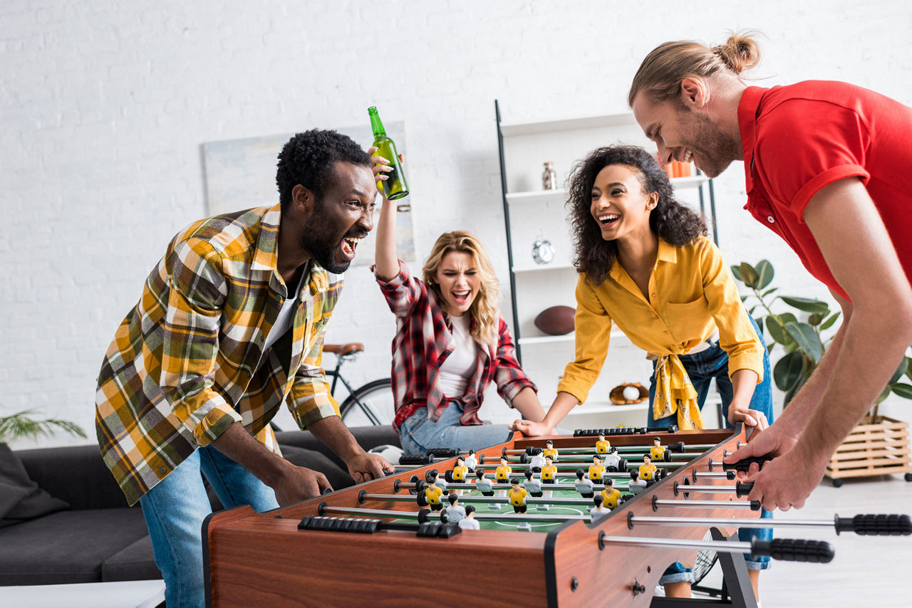 Vier junge und fröhliche Menschen spielen Tischkicker
