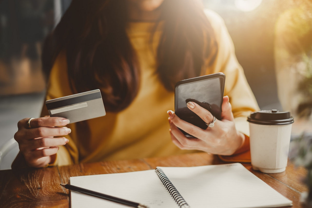 junge asiatische Frau benutzt Smartphone und Kreditkarte um im Cafe online zu shoppen