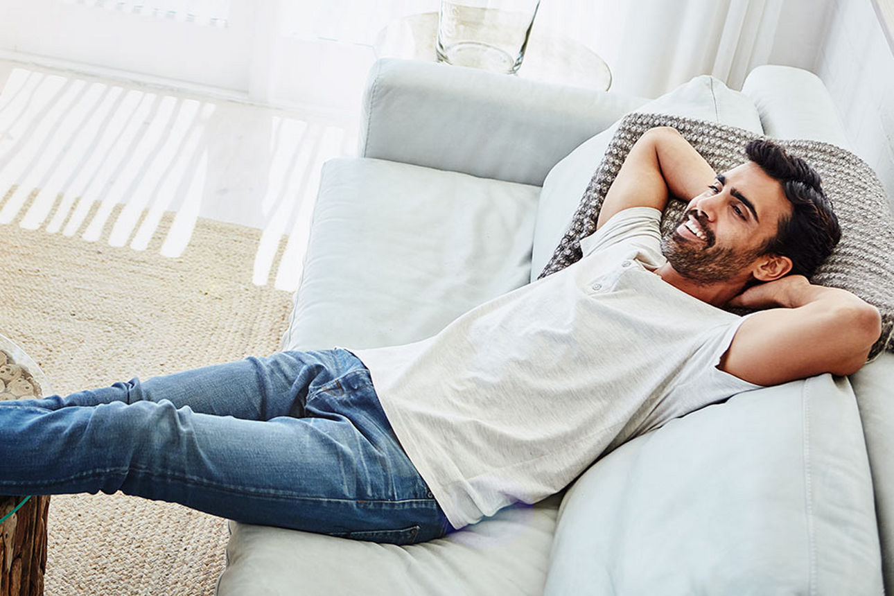 Ein junger Mann liegt entspannt auf einem Sofa und lächelt