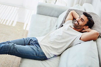 Mann liegt lächelnd auf dem Sofa