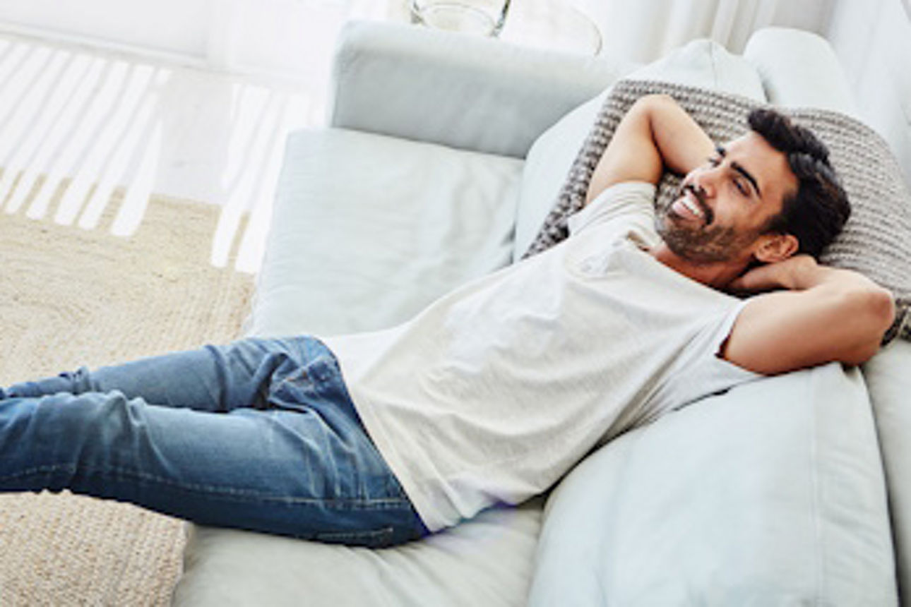 Mann liegt lächelnd auf dem Sofa