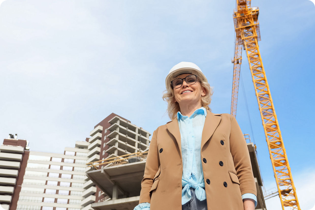 Eine Unternehmerin steht mit Schutzhelm vor einer Baustelle