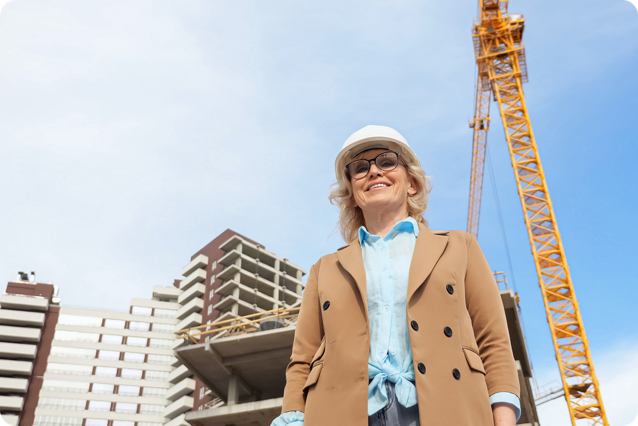 Eine Unternehmerin steht mit Schutzhelm vor einer Baustelle
