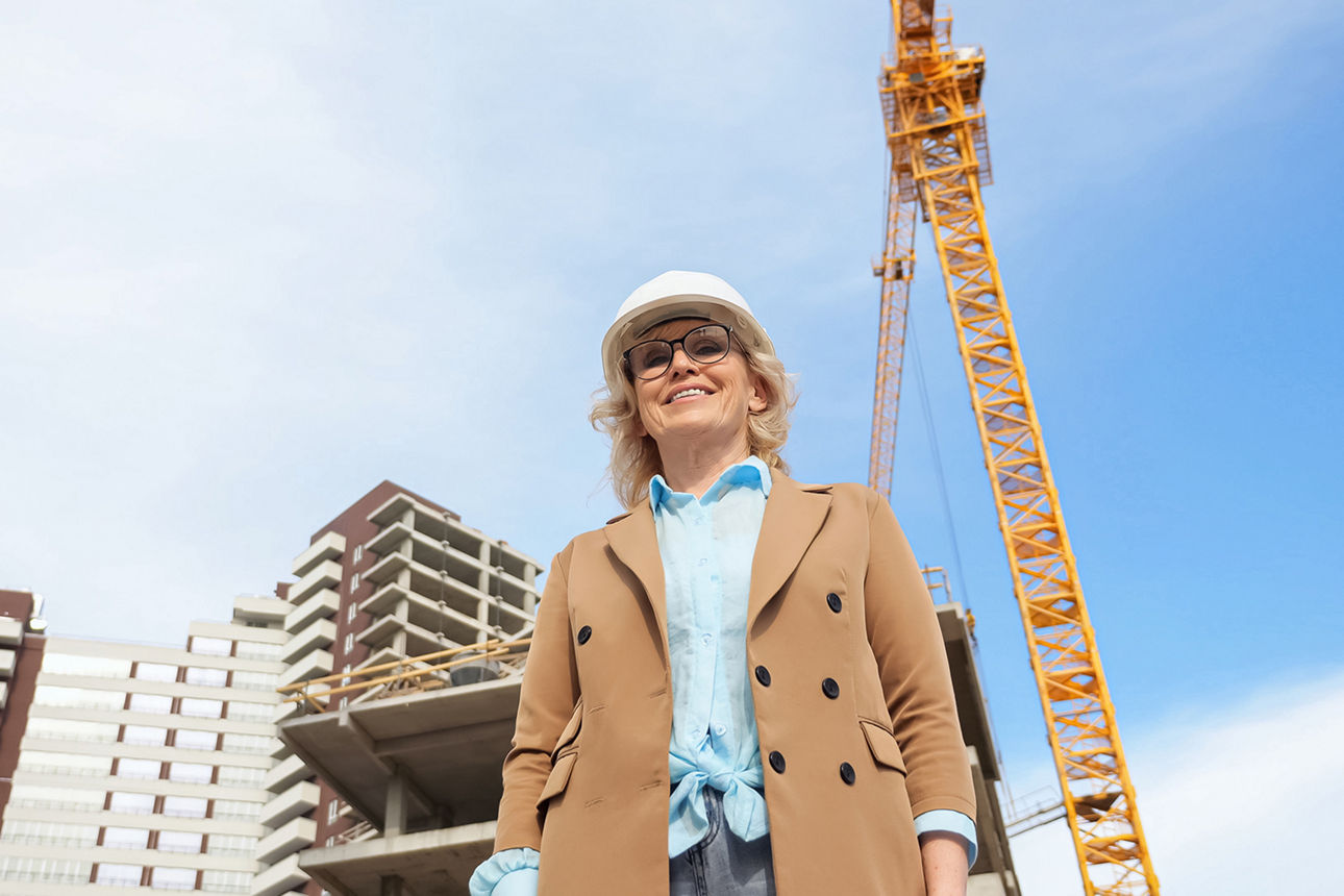 Eine Unternehmerin steht mit Schutzhelm vor einer Baustelle