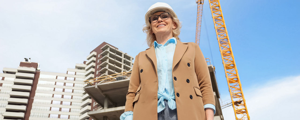Eine Unternehmerin steht mit Schutzhelm vor einer Baustelle