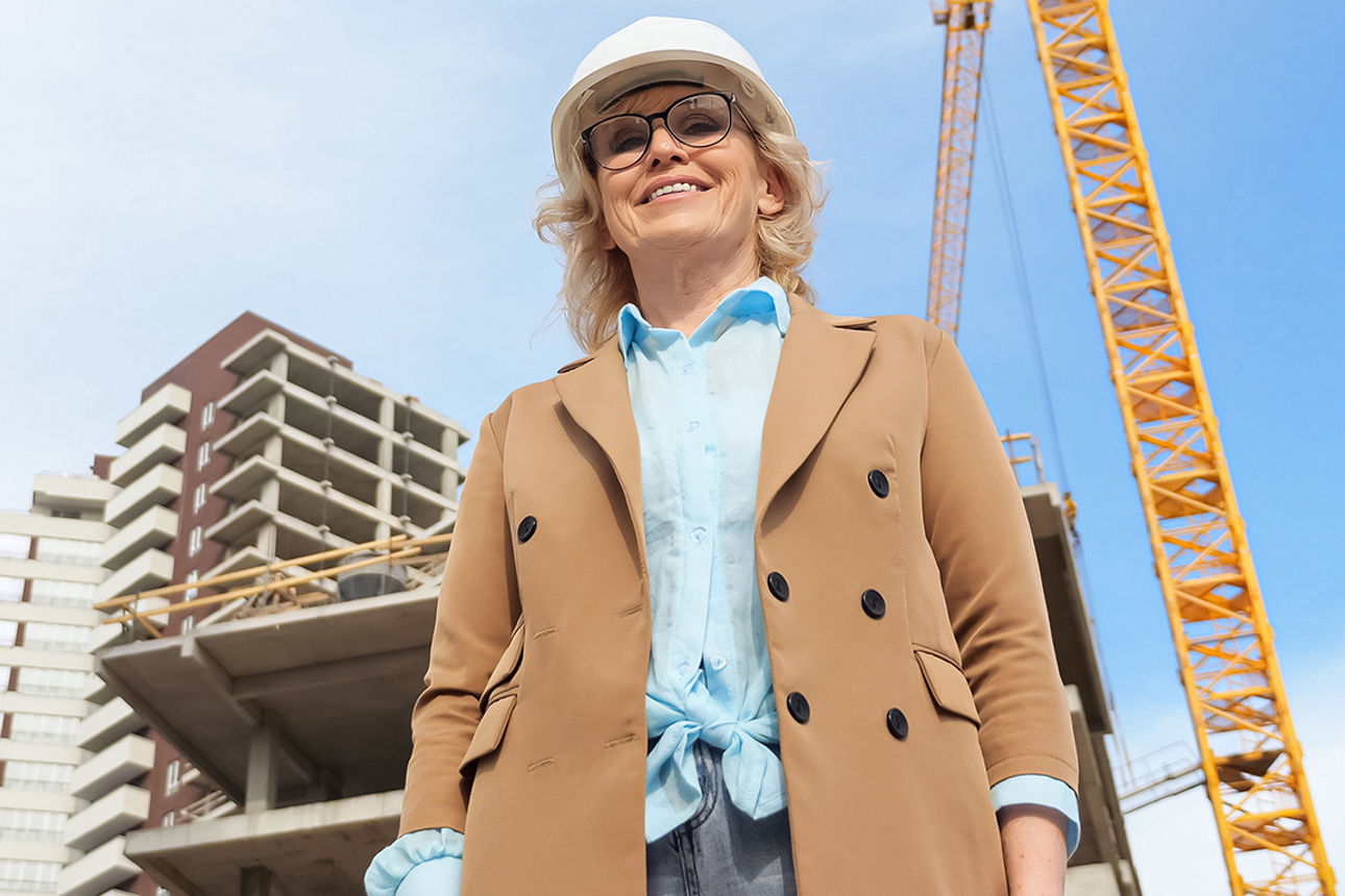 Eine Unternehmerin steht mit Schutzhelm vor einer Baustelle