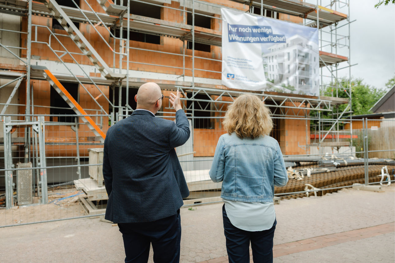 Zwei Personen schauen sich eine Immobilie an die noch im Bau ist, dadrauf ist ein Plakat der Volksbsank Hameln-Stadthagen
