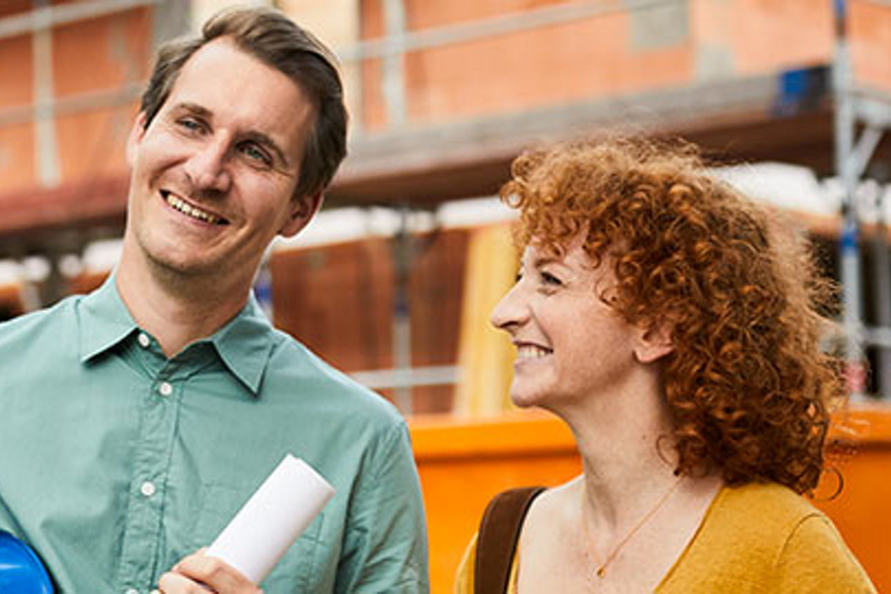 Ein Mann und eine Frau stehen vor einer Baustelle und betrachten die Arbeiten, die im Hintergrund stattfinden