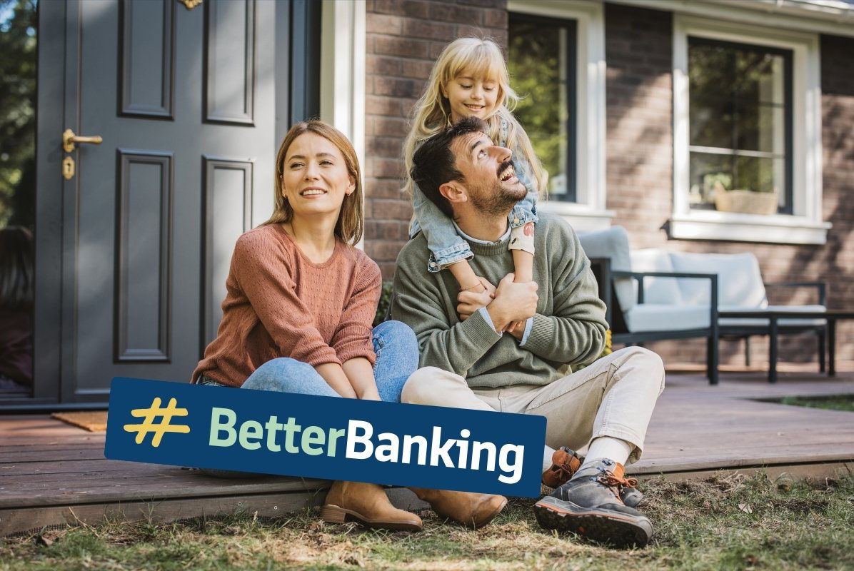 Junges Paar sitzt mit Kind vorm Eingang seines Eigenheims