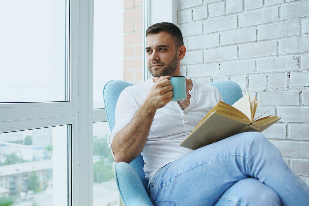 Junger Mann sitzt mit einer Tasse Kaffee im Sessel