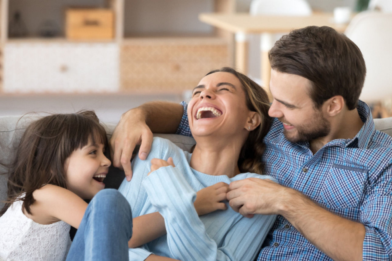 Eine junge Familie sitzt ausgelassen auf dem Sofa im Wohnzimmer