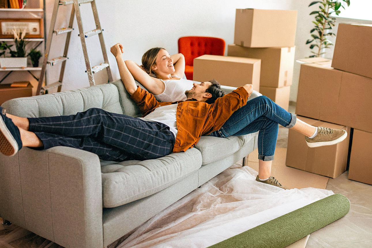 Junges Paar sitzt auf der Couch in ihrer mit Baufinanzierung finanzierten Wohnung