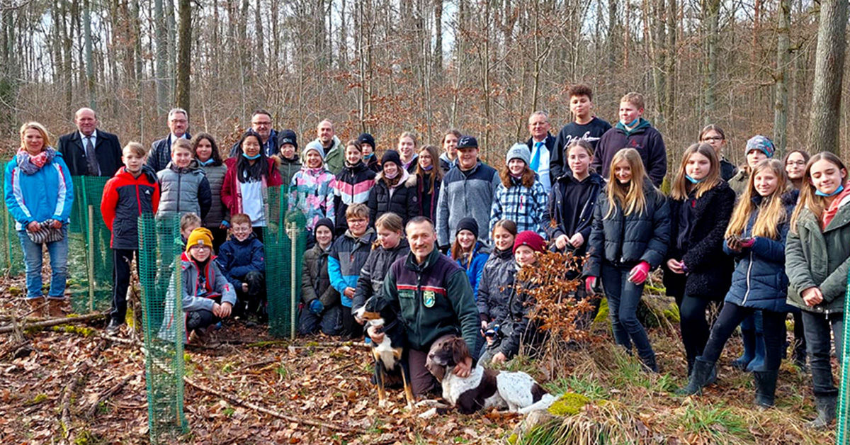 Gruppenbild einer Schulklasse und eines Försters bei der Anpflanzung von neuen Bäumen