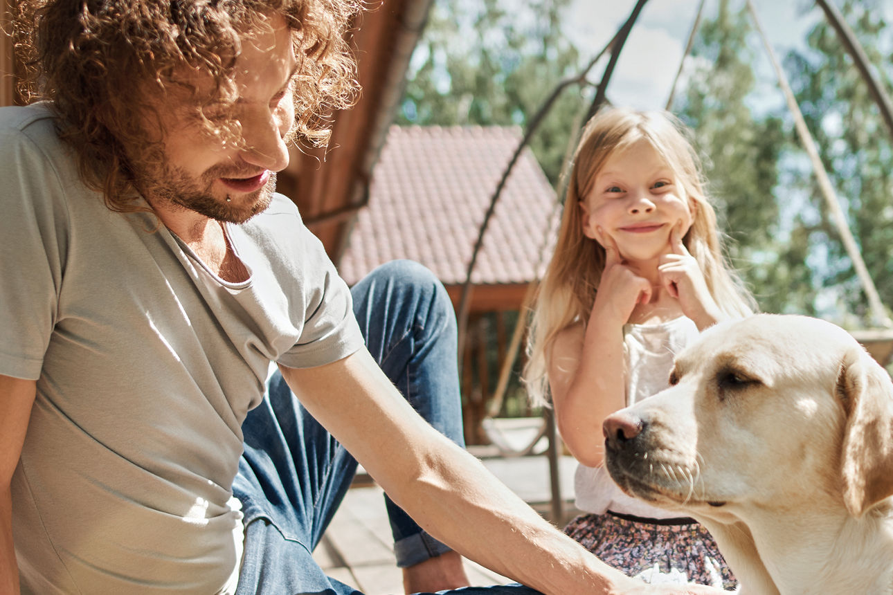 Vater sitzt mit Tochter und Hund vor dem Haus
