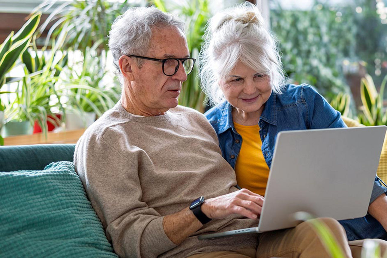 Ein älteres Paar sitzt auf dem Sofa und schaut auf einem Laptop.