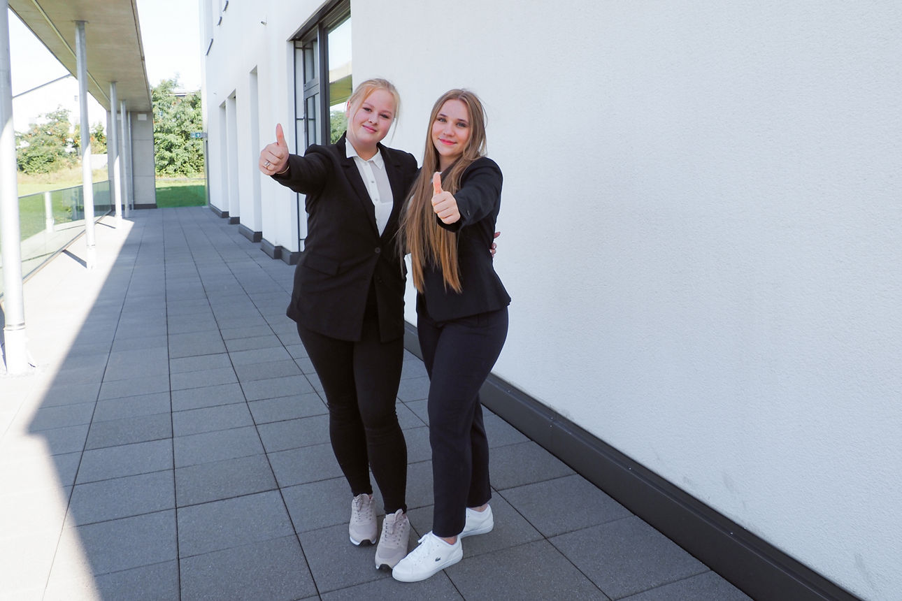 Zwei Kolleginnen stehen lächelnd und mit Daumen nach oben vor der Kamera.