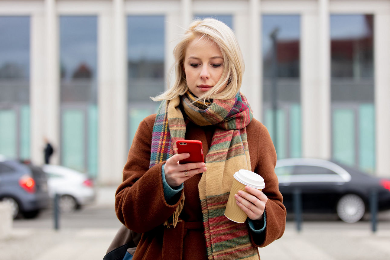 Junge blonde Frau mit Kaffeebecher nutzt Ihr Smartphone