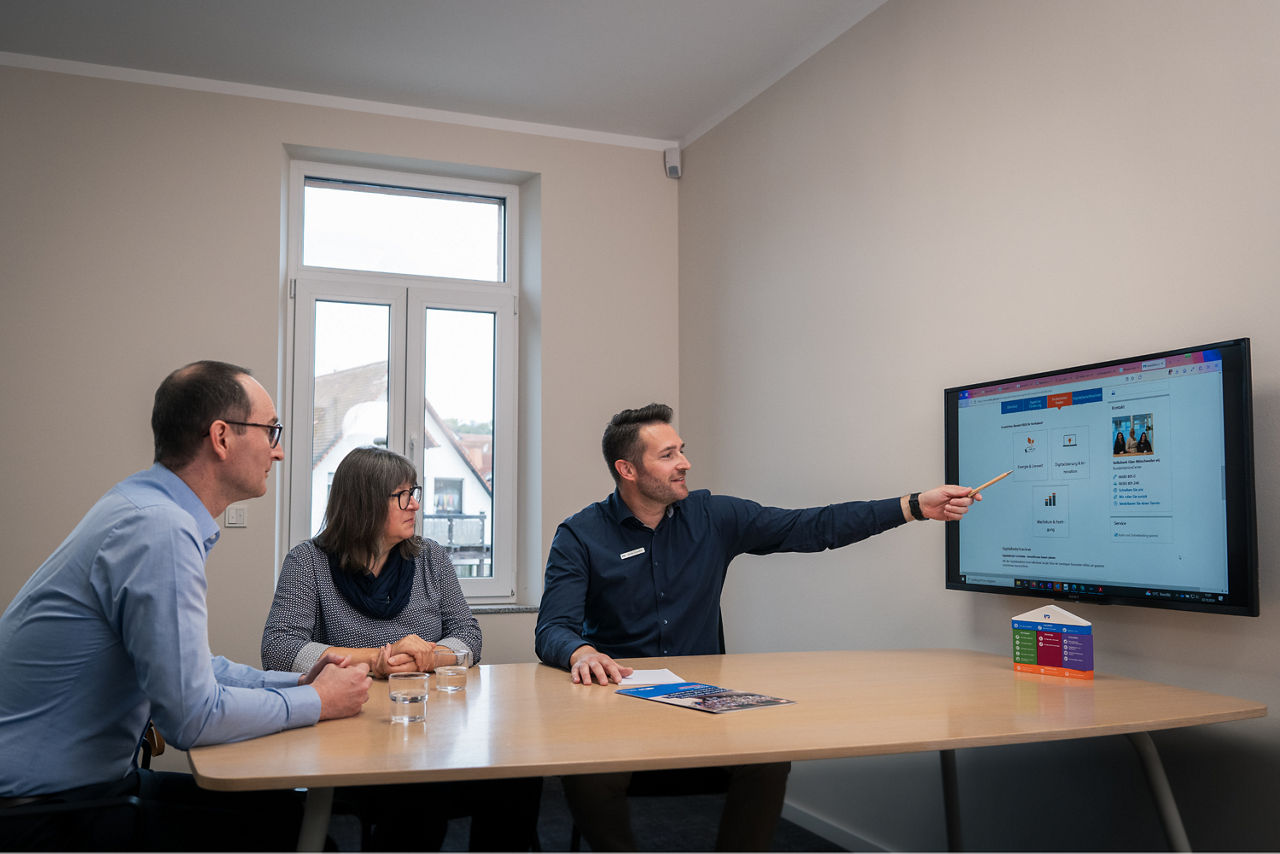 Ein Berater redet mit zwei Kunden in einem Beratungszimmer