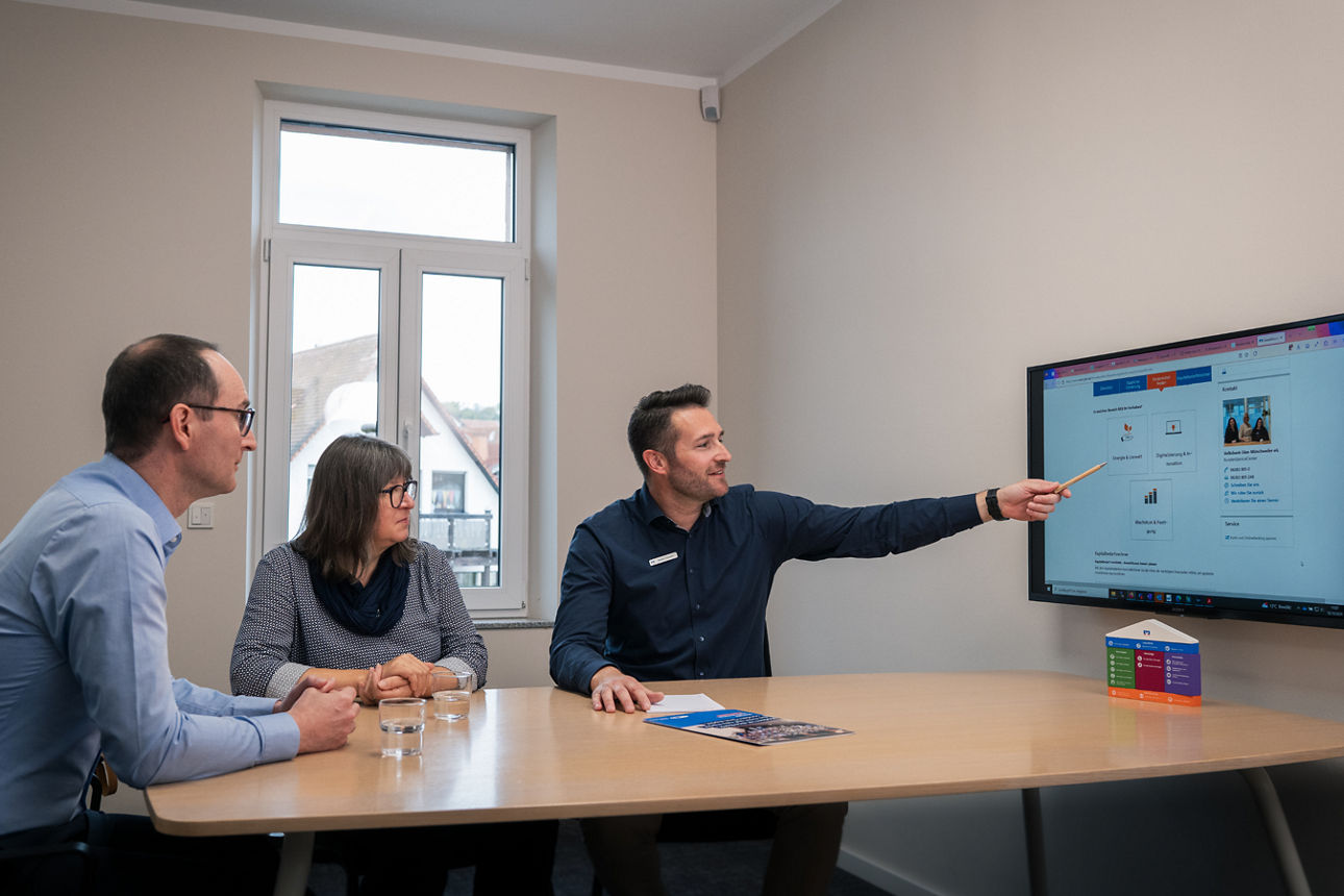 Ein Berater redet mit zwei Kunden in einem Beratungszimmer