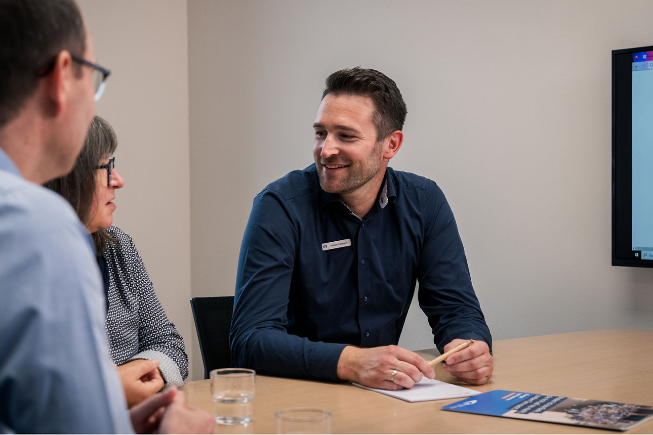 Ein Berater redet mit zwei Kunden in einem Beratungszimmer