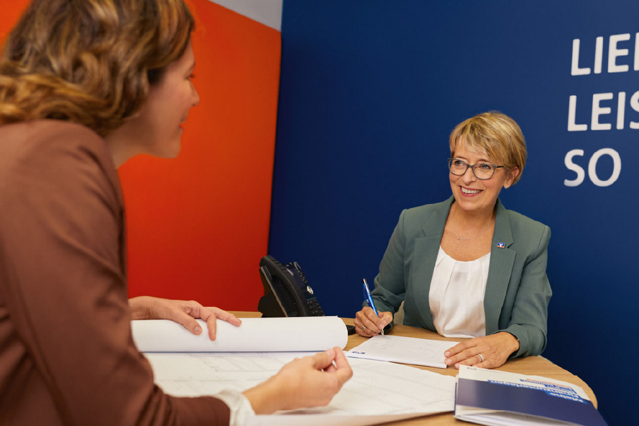 Zwei Frauen befinden sich in einem Beratungsgespräch und sitzen sich lächelnd gegenüber.