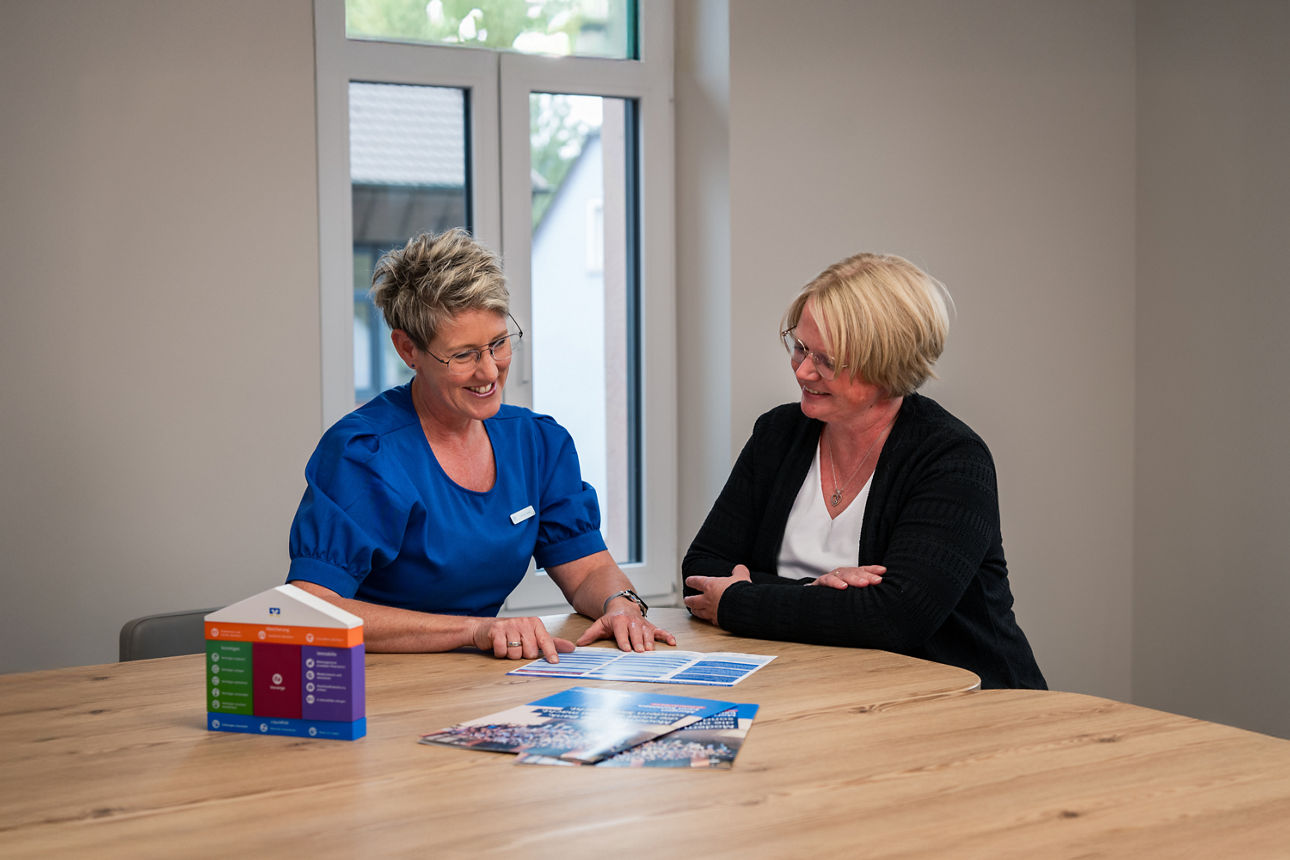 Eine Beraterin erklärt eine Kundin einen Flyer. Dabei sitzen die beiden an einem Tisch
