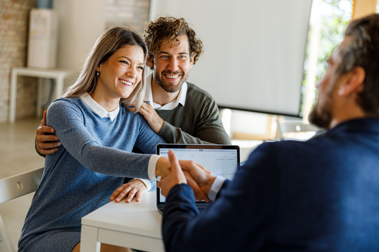 ein junges glückliches pärchen wird von einem Experten zu ihren finanzen beraten