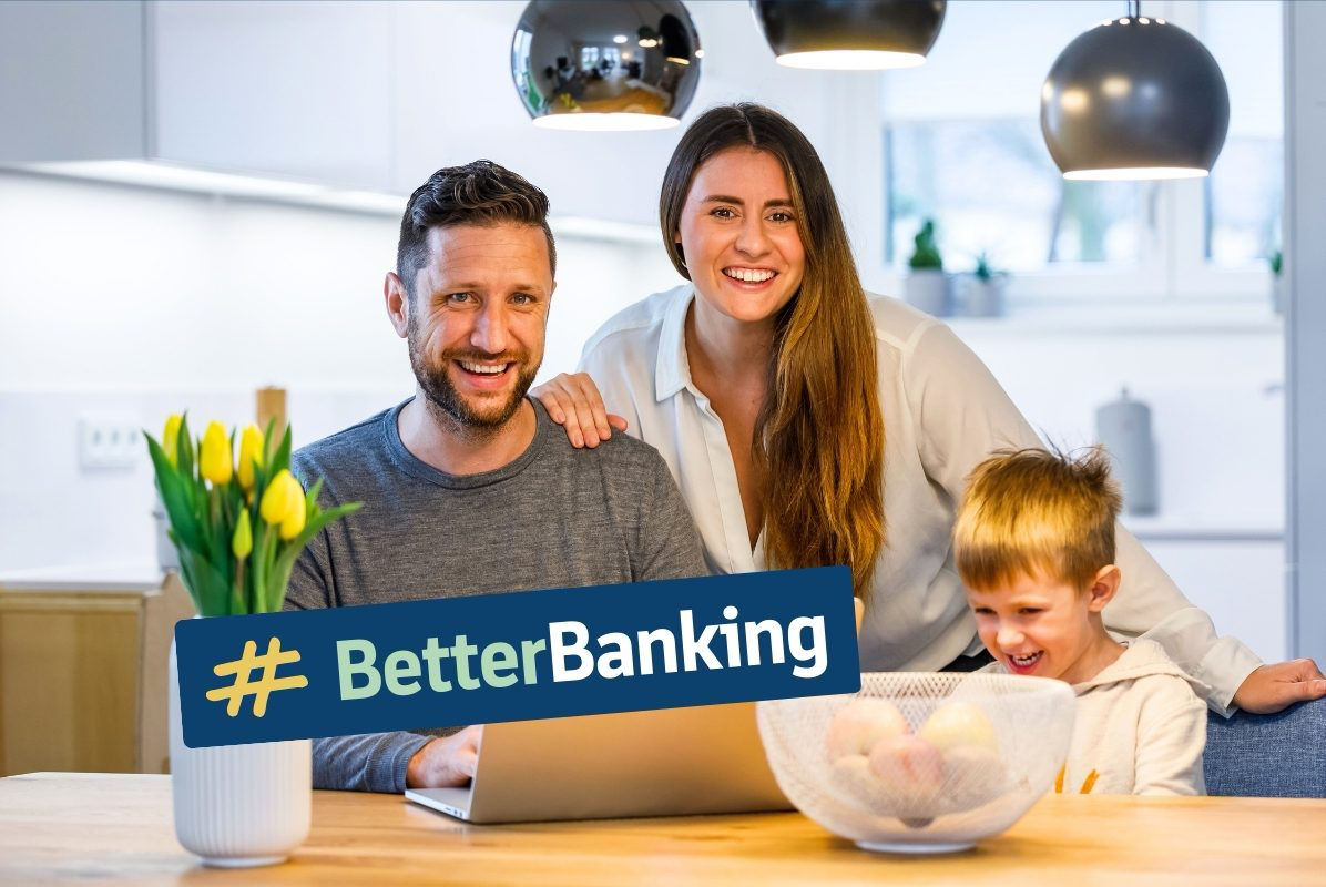 Junges Paar sitzt mit Kind vor Laptop und lächelt in die Kamera