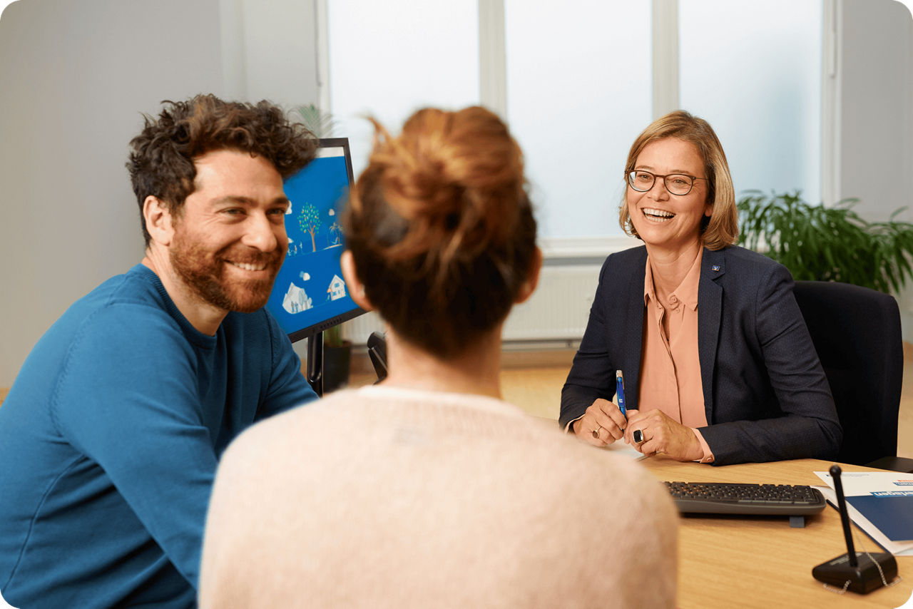 Ein Paar und eine lachende Bankberaterin in einem Gespräch.