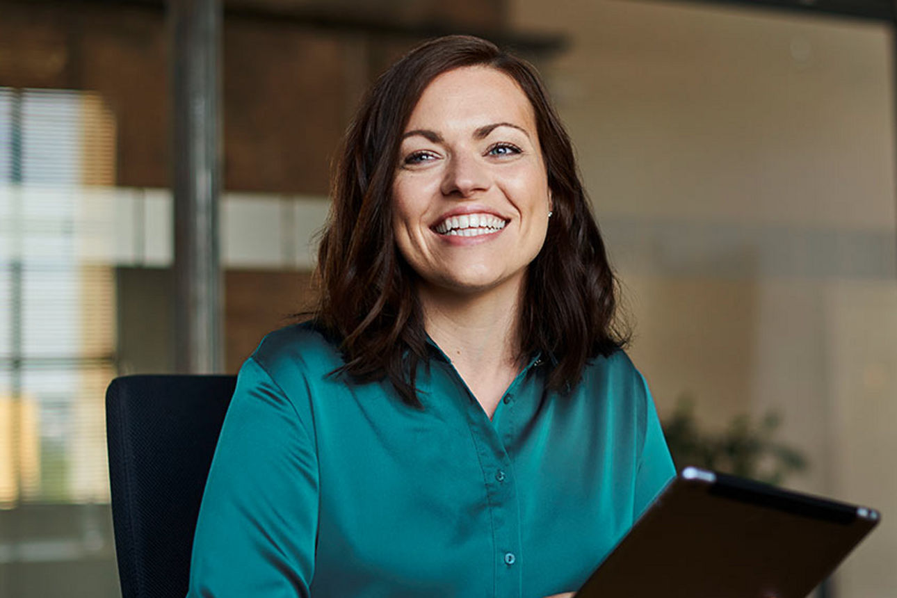 Junge Frau lächelt und hat ein Tablet in der Hand.