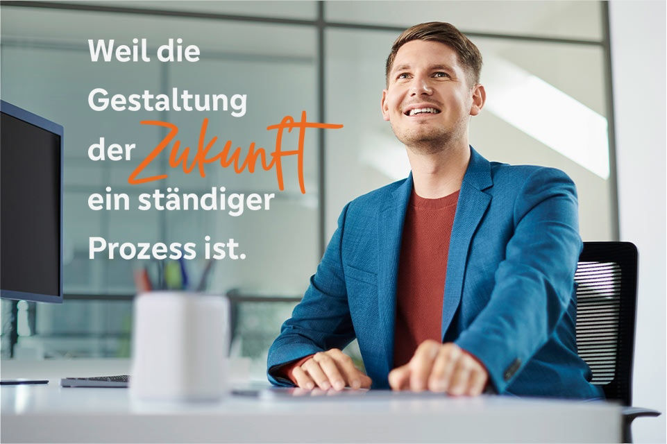 Ein junger Mann sitzt lächelnd am Schreibtisch