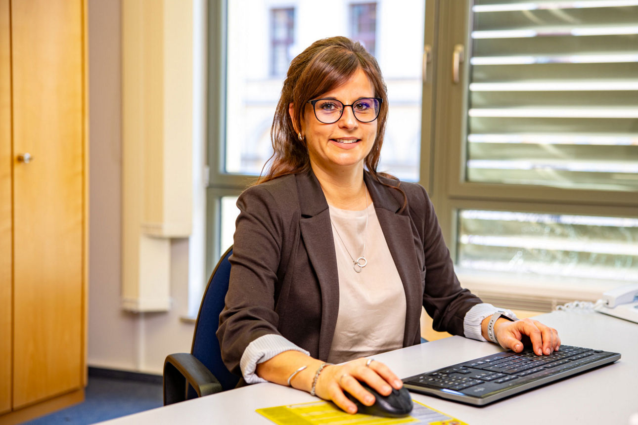 Eine Frau sitzt lächelnd am Arbeitsplatz in der Bank