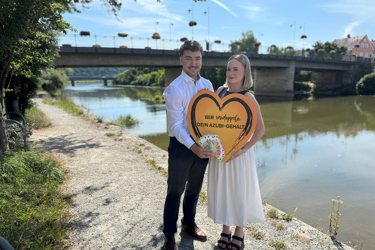 Ein junger Mann und eine junge Frau stehen an einem Fluss und halten ein Schild in den Händen