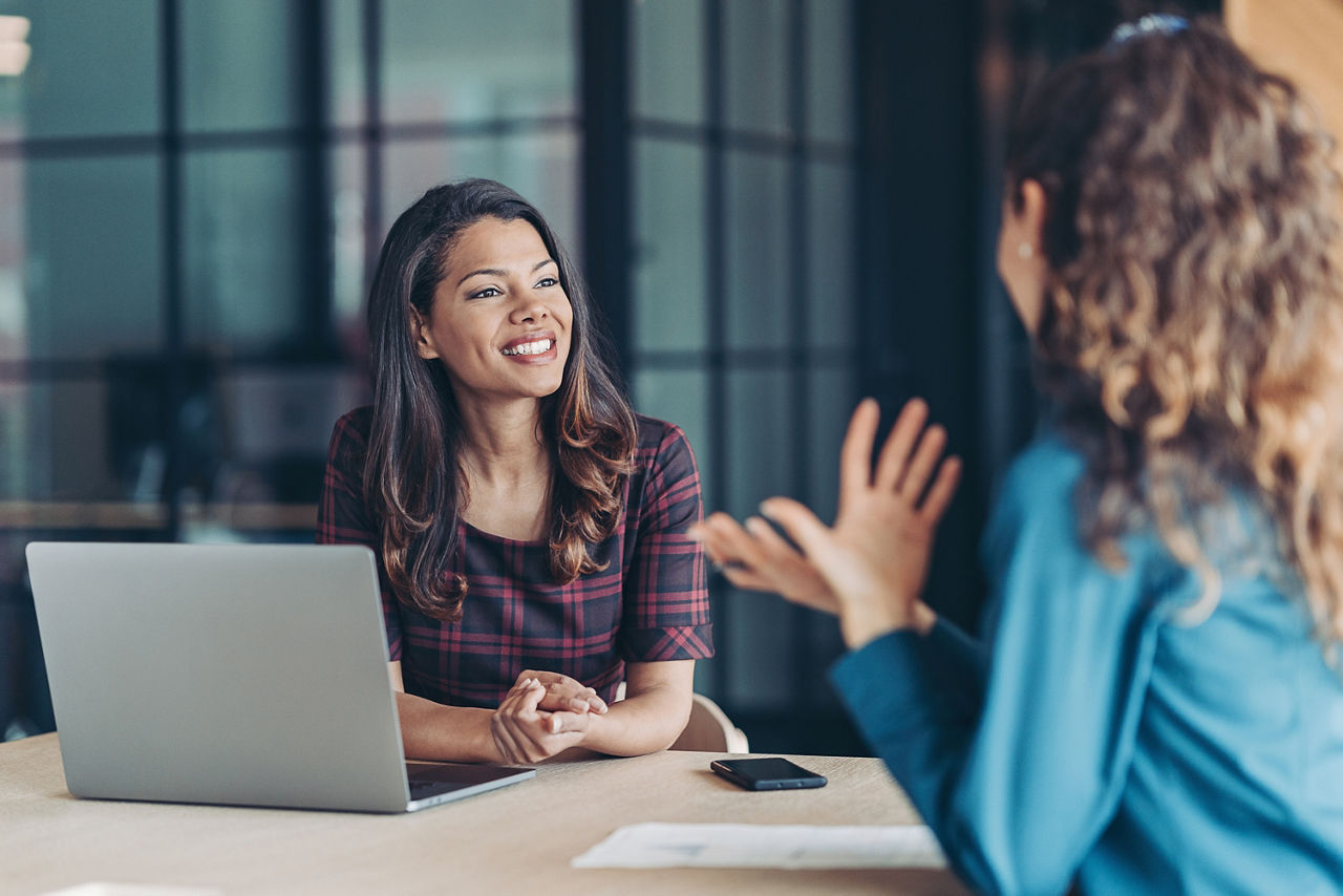 Zwei Frauen sitzen im Büro und unterhalten sich über relevante Arbeitsthemen