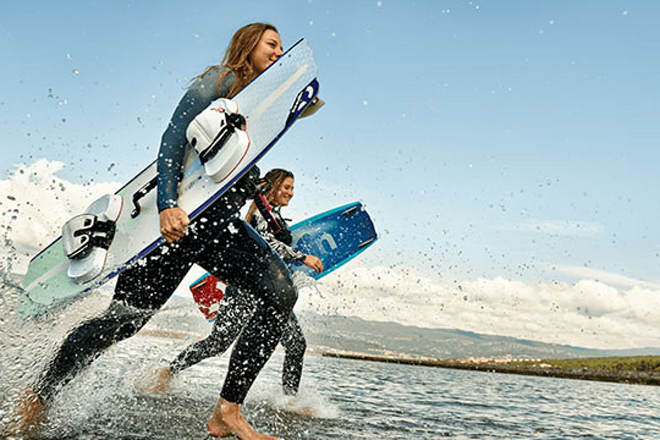 Zwei Personen mit Wake Board laufen durchs Wasser.