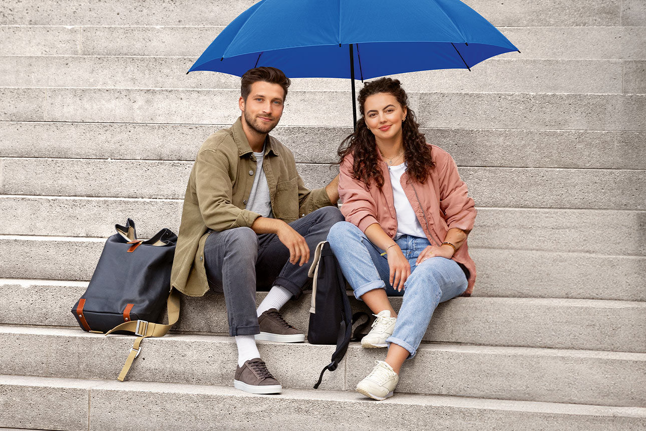 Mann und Frau sitzen auf einer Treppe mit einem blauen Regenschirm in der Hand 