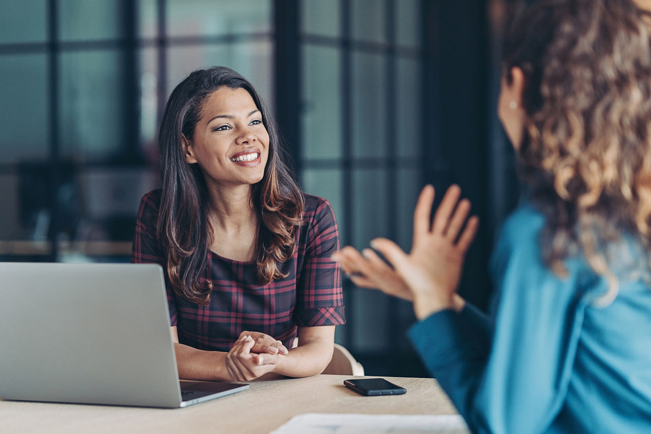 Zwei Frauen sitzen im Büro und unterhalten sich über relevante Arbeitsthemen