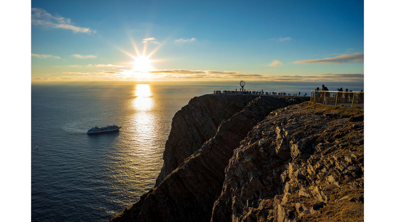 Sonnenuntergang am Nordkap-Plateau. Der Globus steht auf der Klippe, das Licht der Mitternachtssonne reflektiert auf dem Meer.