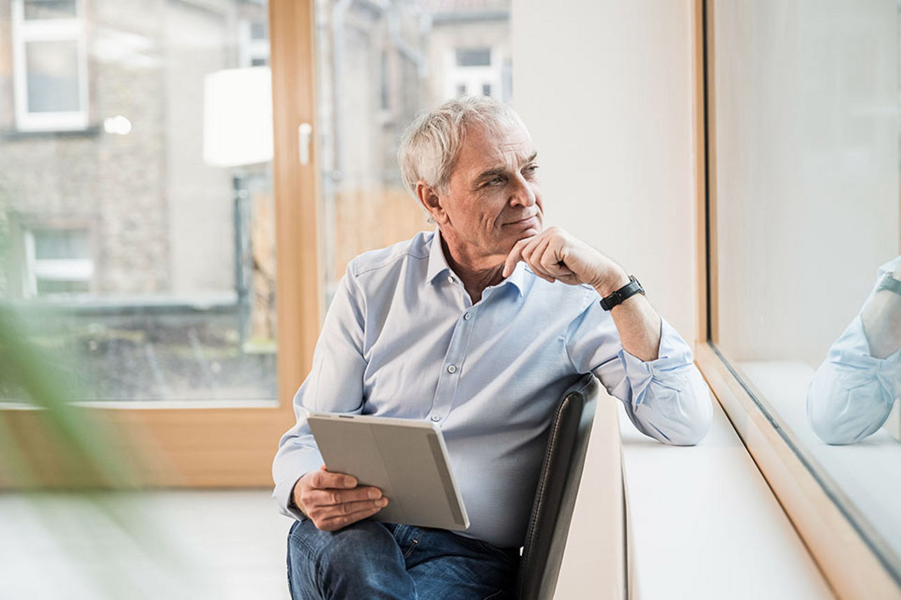 Ein Mann mit einem Tablet in der Hand schaut aus dem Fenster