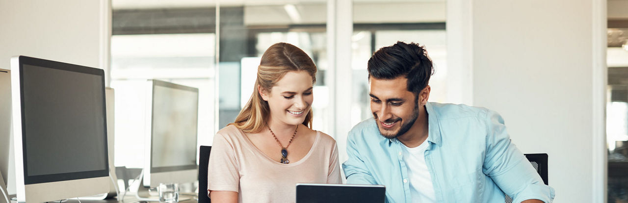 Eine Mann mit blauem Hemd und eine Frau schauen interessiert auf ein Laptop