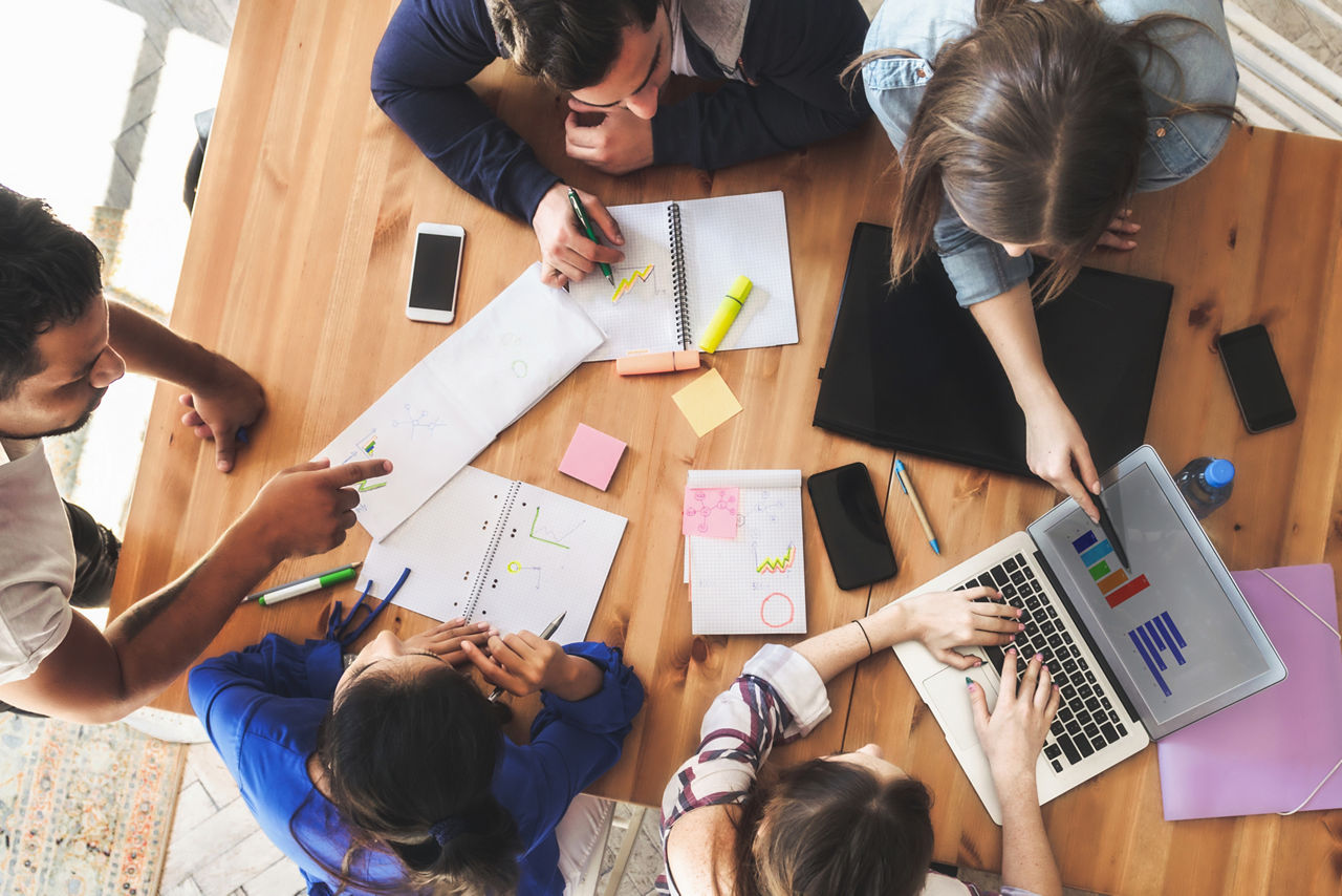 Fünf Geschäftsleute sitzen an einem runden Tisch und unterhalten sich über verschiedene Finanzierungen für Betriebsmittel