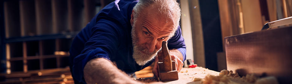 Ein älterer Mann arbeitet konzentriert an einem Holzstück