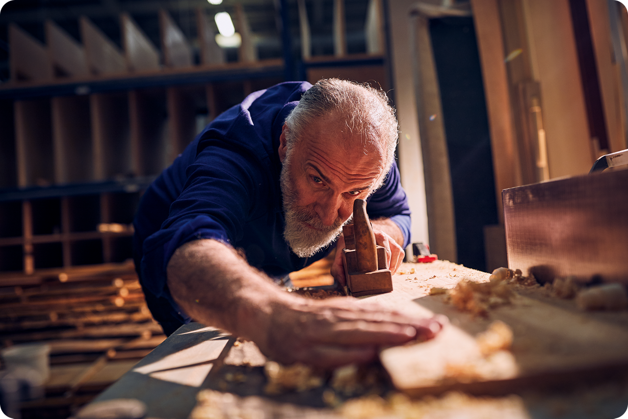 Ein Schreiner steht an seiner Werkbank und hobelt