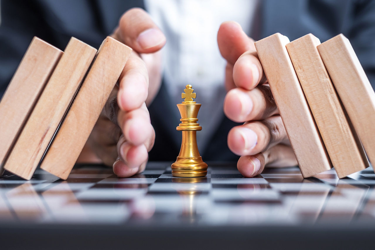 Geschäftsmann Hand schützen Schach-König Figur und Stoppen fallender Holzklötze oder Dominosteine. Geschäft, Risikomanagement, Lösung, wirtschaftliche Regression, Versicherung, Strategie und Unterbrechungskonzepte
