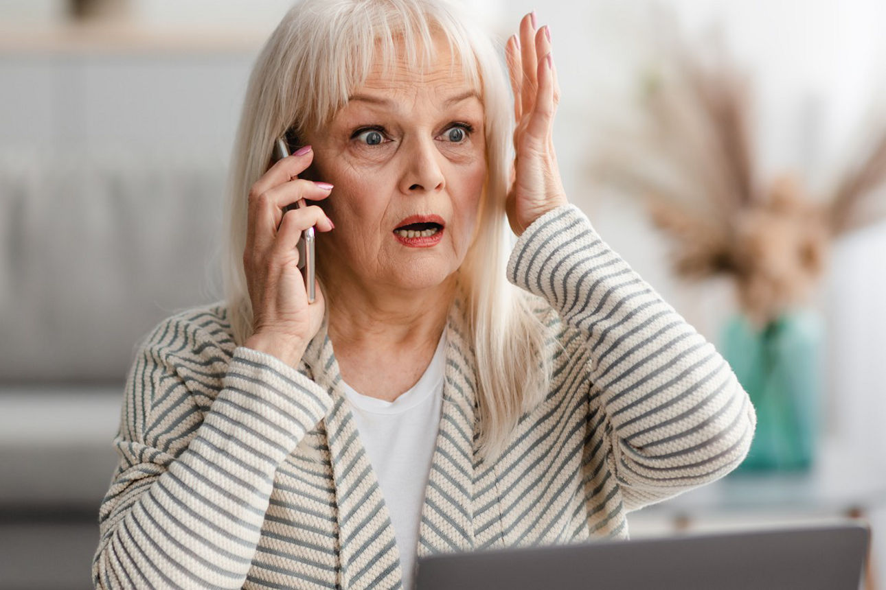 Eine entsetzt schauende Frau telefoniert. In der rechten Hand das Smartphone - die linke Hand hält sie an ihren Kopf.
