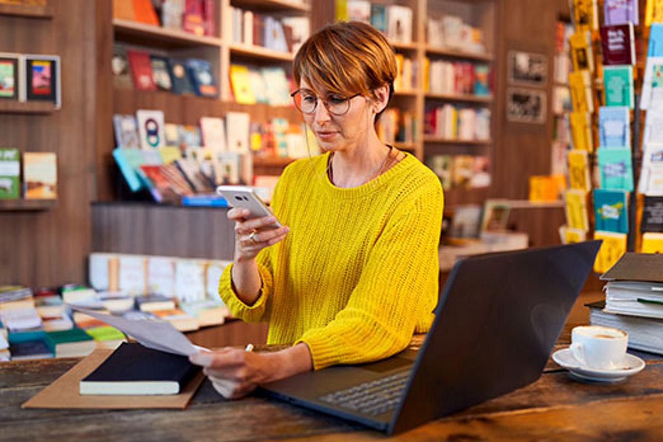 Mitarbeiterin in einer Buchhandlung schaut auf ihr Smartphone