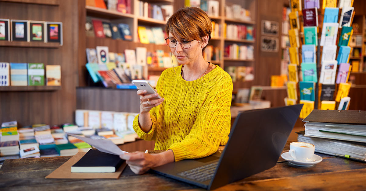 Mitarbeiterin in einer Buchhandlung schaut auf ihr Smartphone