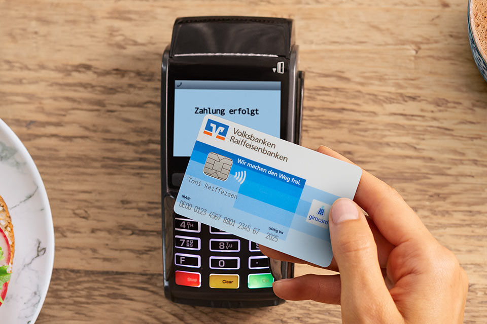 Eine Person hält eine girocard (Debitkarte) vor ein Kartenlesegerät