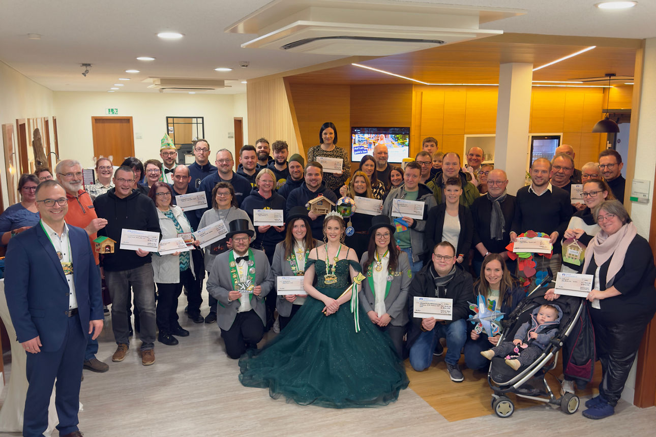 Spendenübergabe in der Bankfiliale. Eine große Gruppe Menschen hat sich aufgereiht.