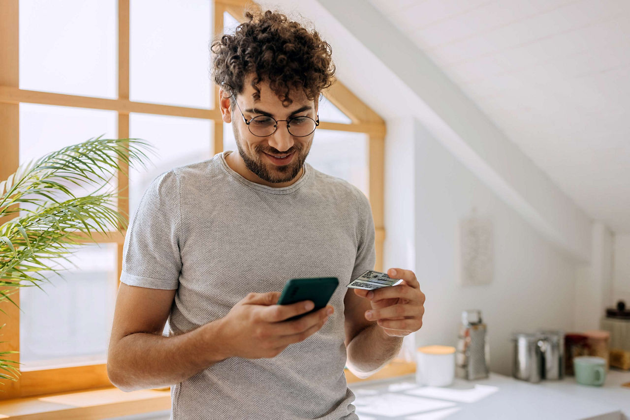 Mann schaut auf sein Smartphone während er eine Karte in der Hand hält
